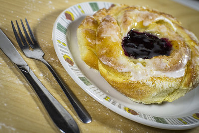 The danish was phootgraphed on top of a wooden board with a 50mm lens @ F1.2. The wood, fork and plate were props that gave this photo a &quot;at home&quot; feeling. We sprinkled flour on the board for added effect. The lighting is two LED softboxes. The white balance is set warm to match the browns of the danish and the wood.